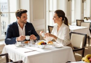 Muž a žena majú raňajky v moderne zariadenej hotelovej jedálni pri stole s kávou a ovocím.