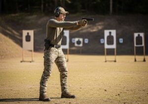 Osoba na vonkajšej strelnici s ochranou očí a sluchu drží pištoľ smerom k terčom.