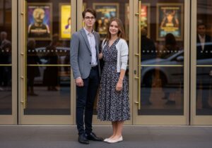 Mladý pár v elegantnom oblečení stojí pred moderným divadlom večer, s úsmevom a istotou.